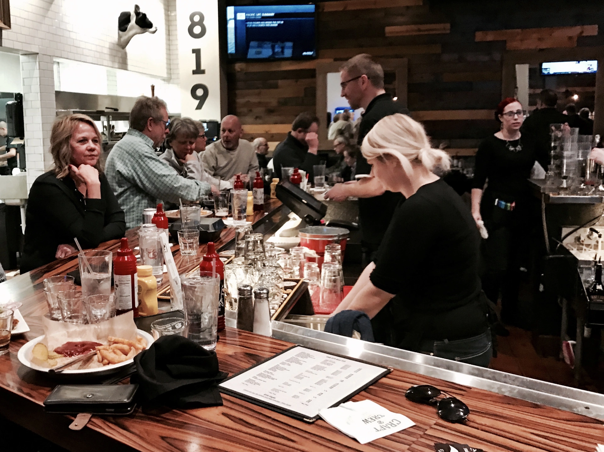 Diners at a busy restaurant bar with 78 Brand ketchup bottles on the counter